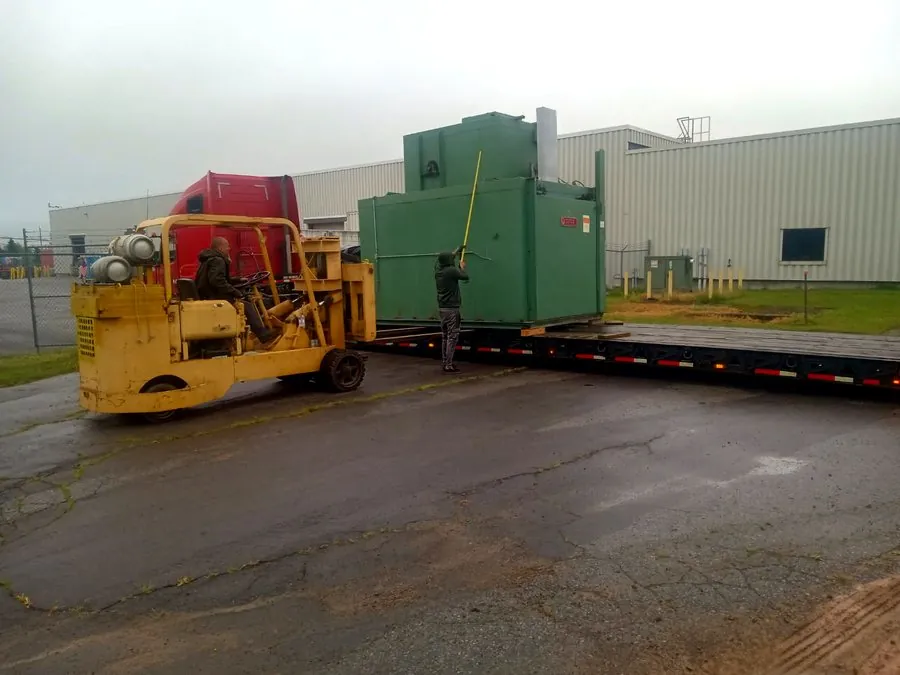 Forklift loading industrial equipment onto a lowboy trailer